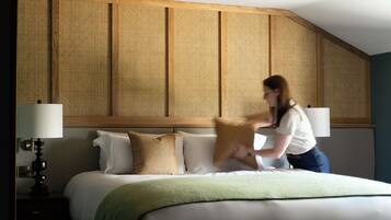 A hotel room with a large bed, a wooden headboard, and a green throw blanket.