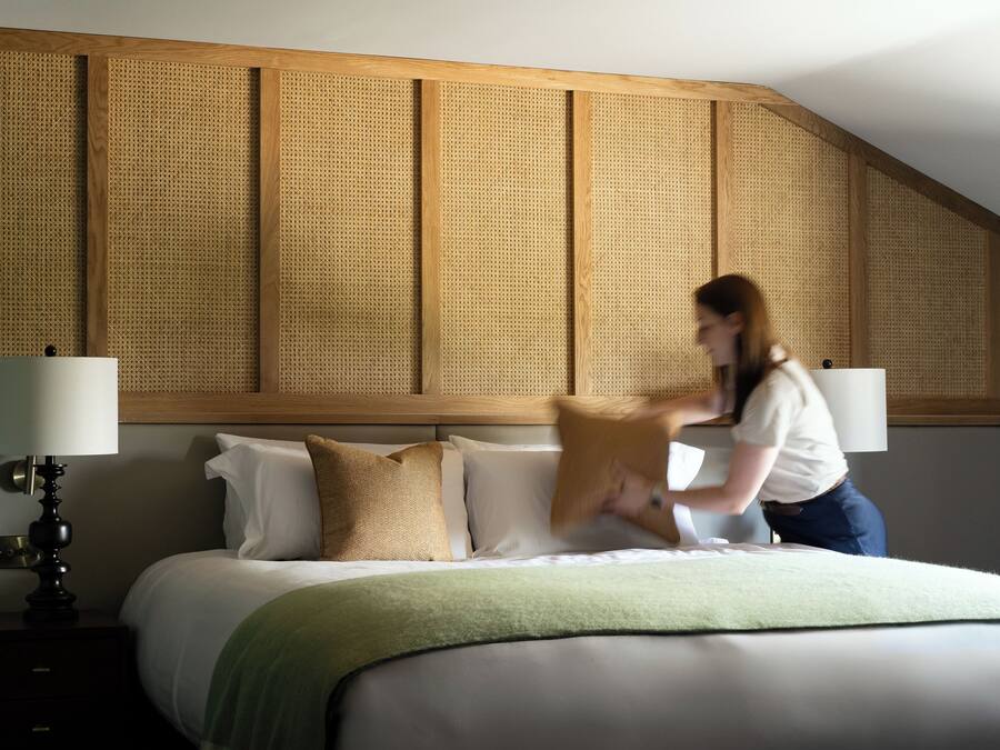 A hotel room with a large bed, a wooden headboard, and a green throw blanket.