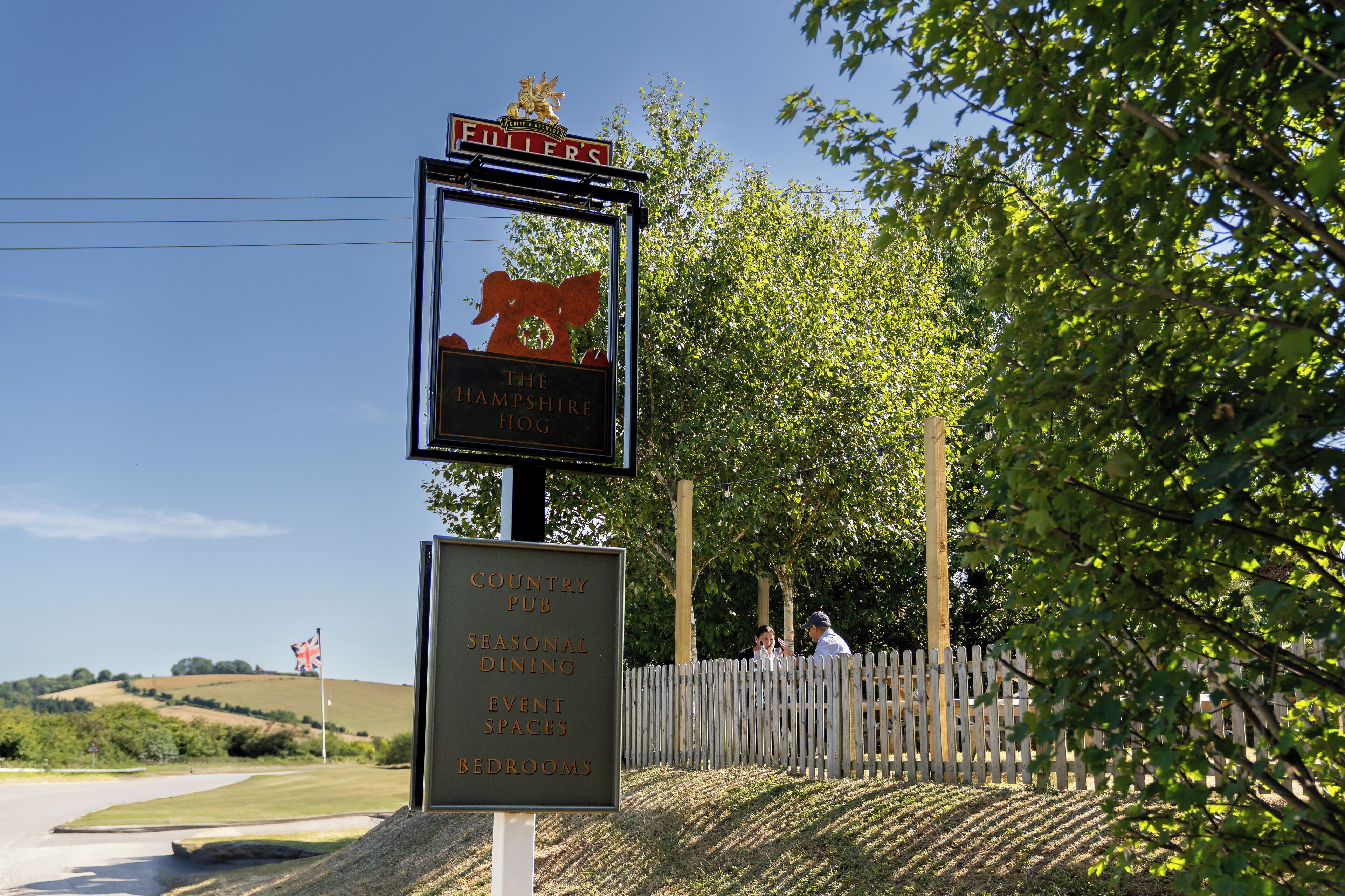 Tabella di segnaletica per The Hampshire Hog, che indica servizi come pub di campagna, ristorazione stagionale, spazi per eventi e camere da letto.
