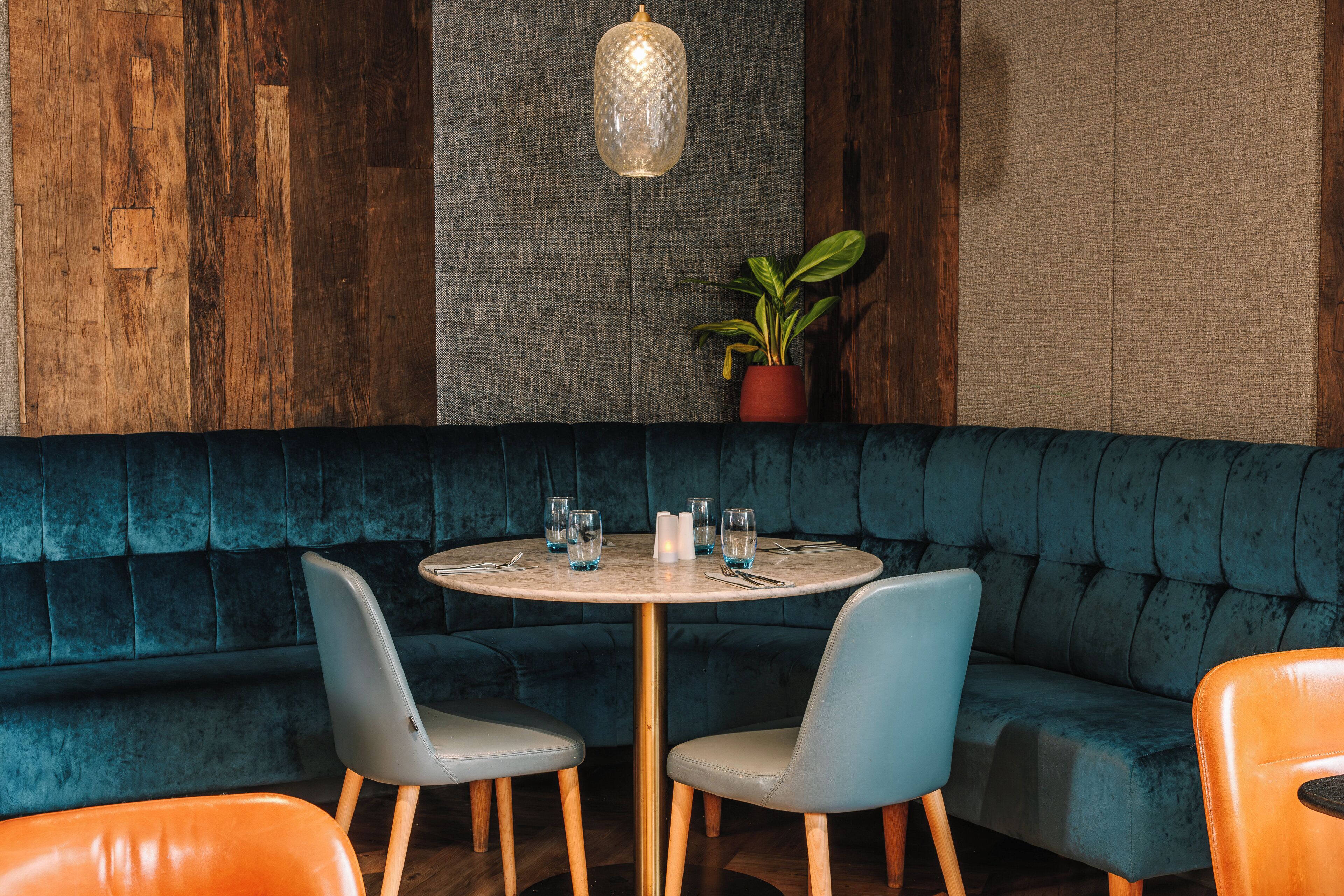 Un rincón comedor acogedor con una mesa redonda, dos sillas, una planta en maceta y un banco tapizado en azul.