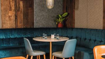 Un rincón comedor acogedor con una mesa redonda, dos sillas, una planta en maceta y un banco tapizado en azul.