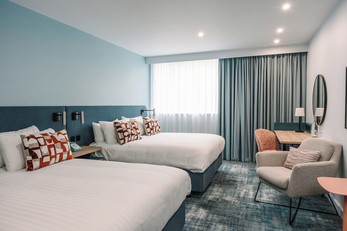 A hotel room with two beds, a desk, a chair, and a large window with curtains.