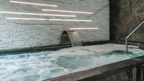 Un espace spa agrémenté d’un mur en pierre, d’un sol carrelé et d’un élément décoratif aquatique avec une cascade.