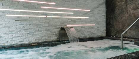 A spa area with a stone wall, a tiled floor, and a water feature with a waterfall.