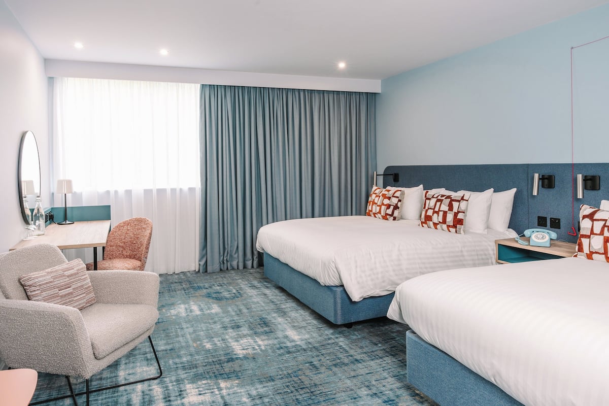 A hotel room with two beds, a desk, a chair, and a large window with curtains.