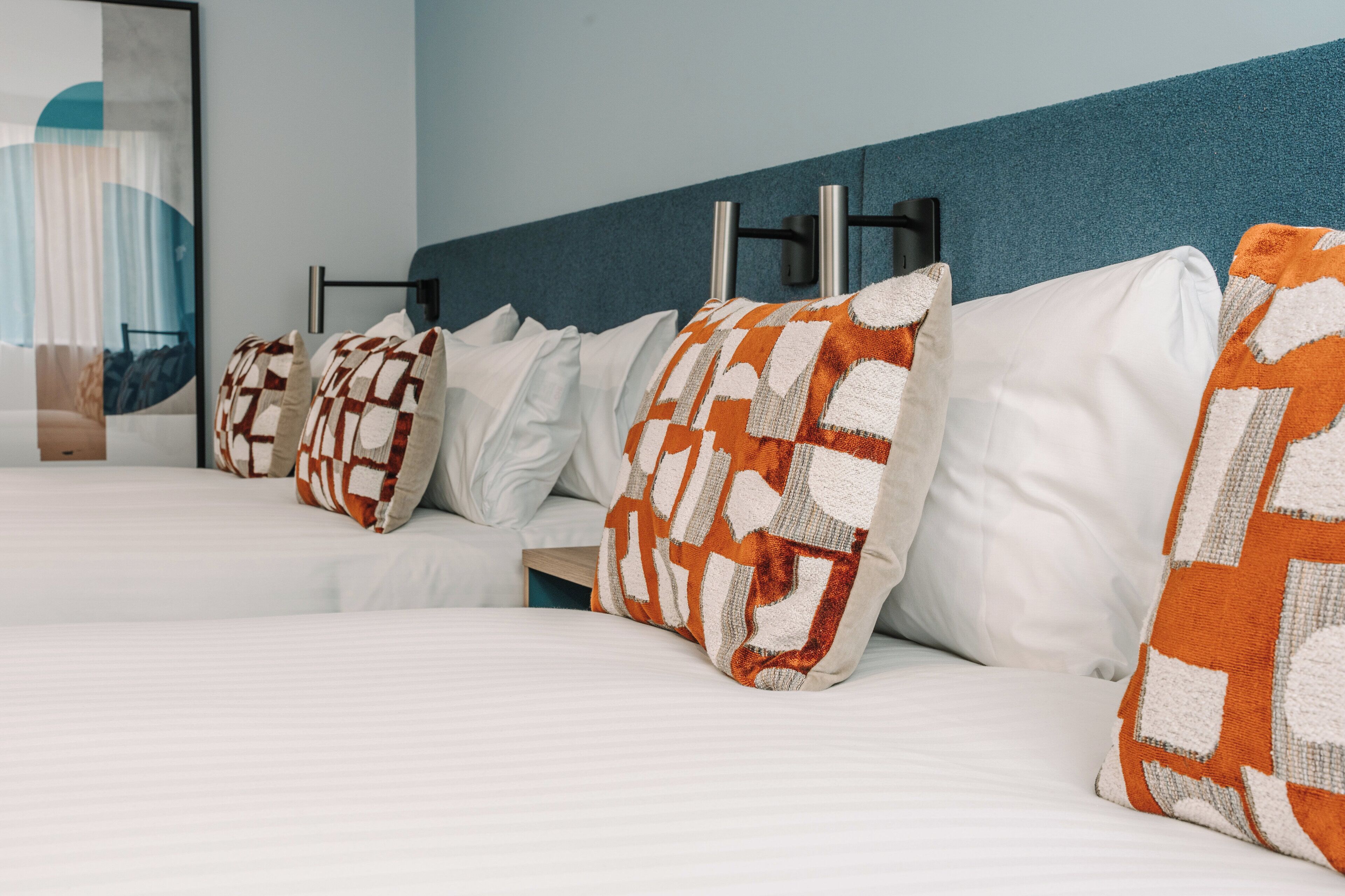 Una habitación de hotel con cama, ropa de cama blanca y almohadas con estampado naranja y blanco.