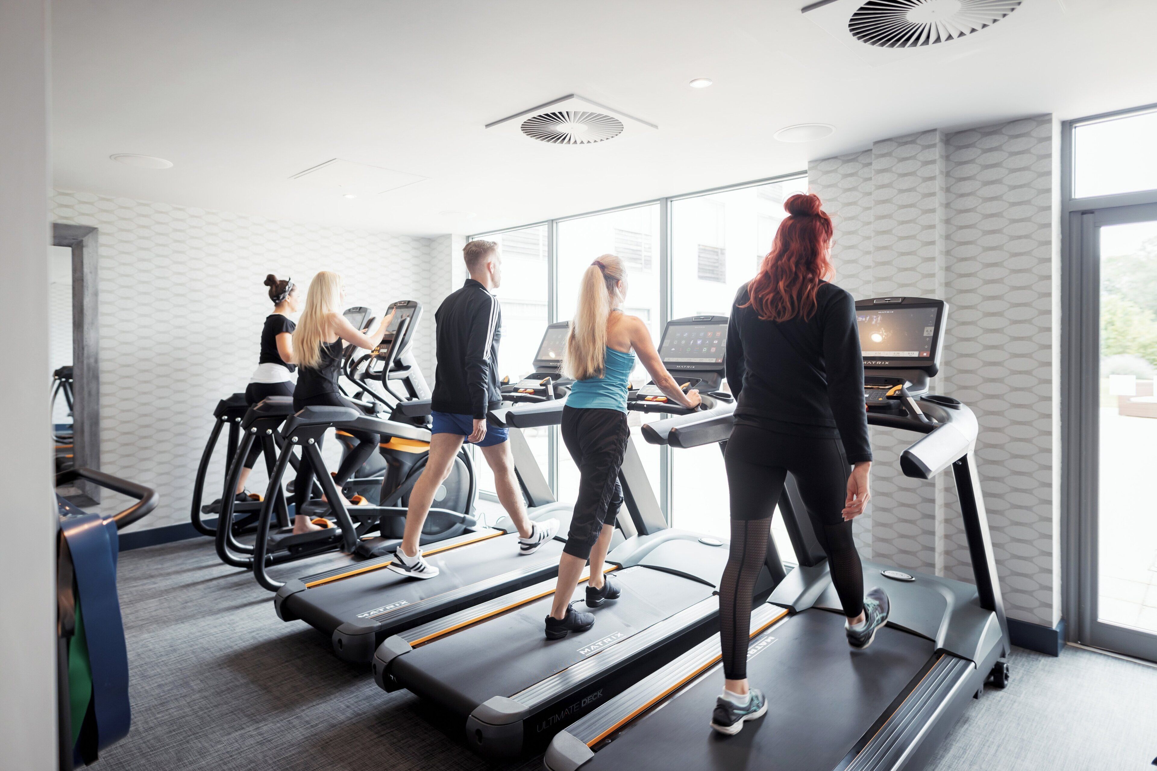 A fitness center with treadmills, a wall-mounted screen, and a patterned wall.