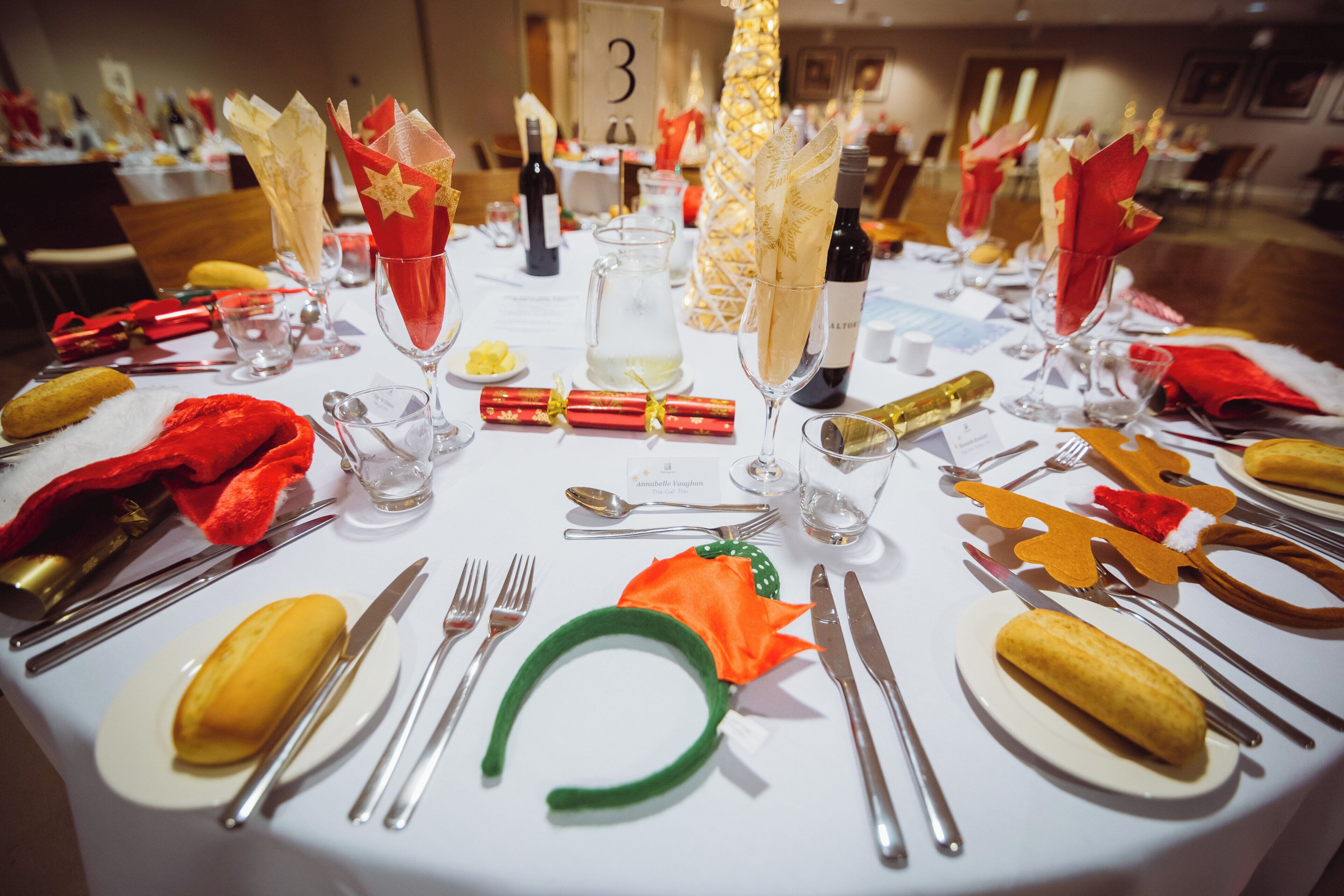 A round dining table set for a formal meal with multiple place settings, including plates, cutlery, and glassware.