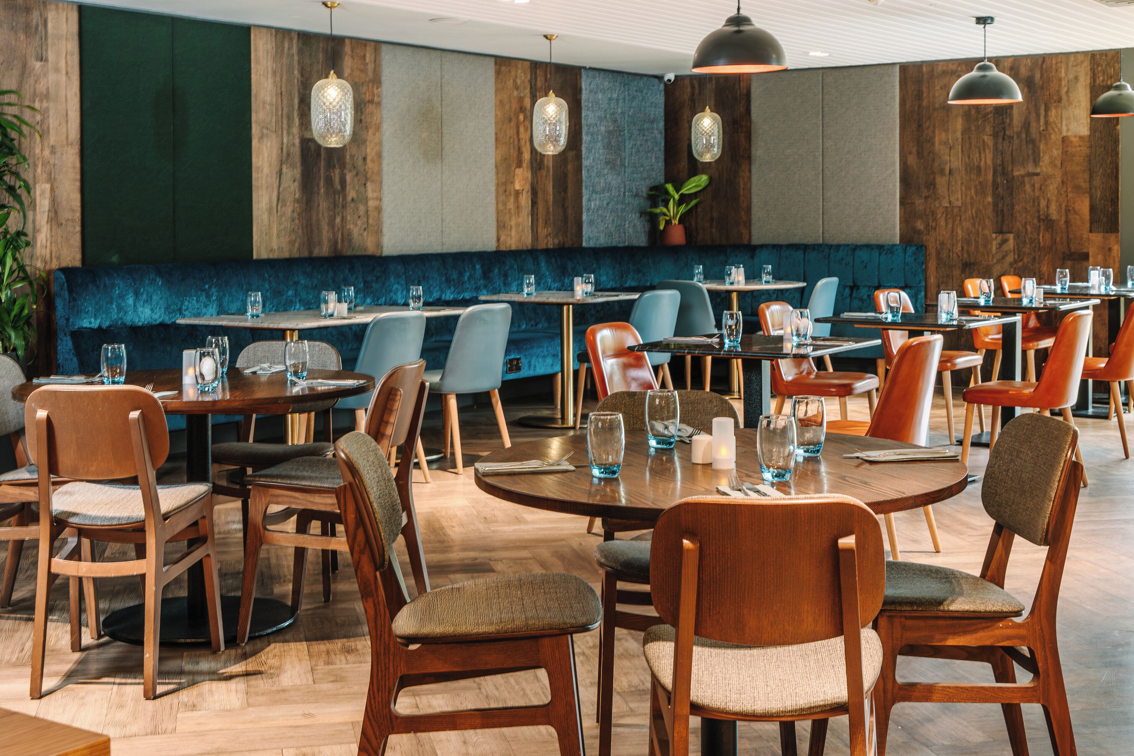 Ein Restaurant mit Holztischen und -stühlen, blau gepolsterten Sitzbänken und hängenden Pendelleuchten.