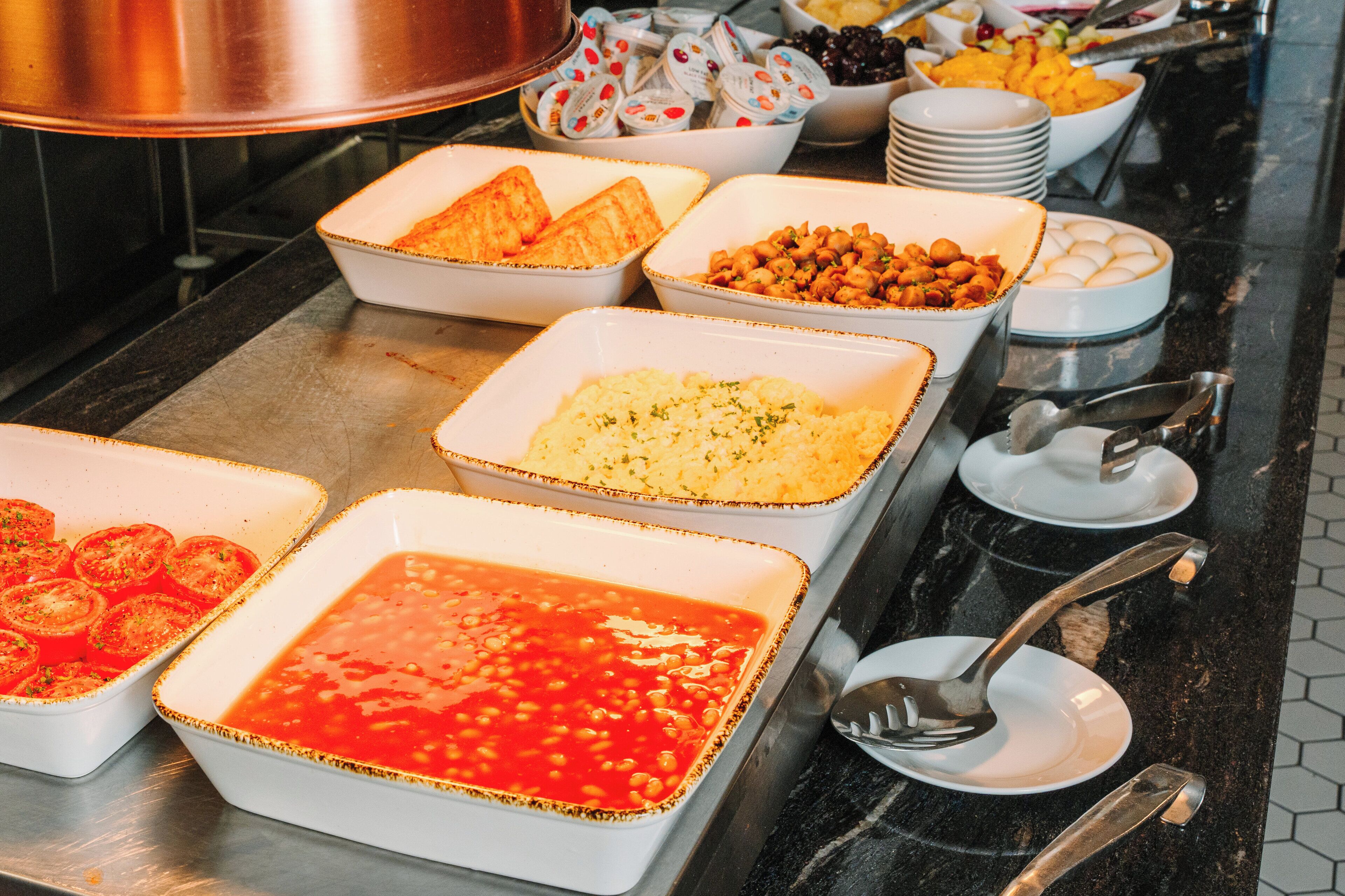 Un buffet proposant une variété de plats, notamment des tomates, des haricots et d’autres aliments préparés.
