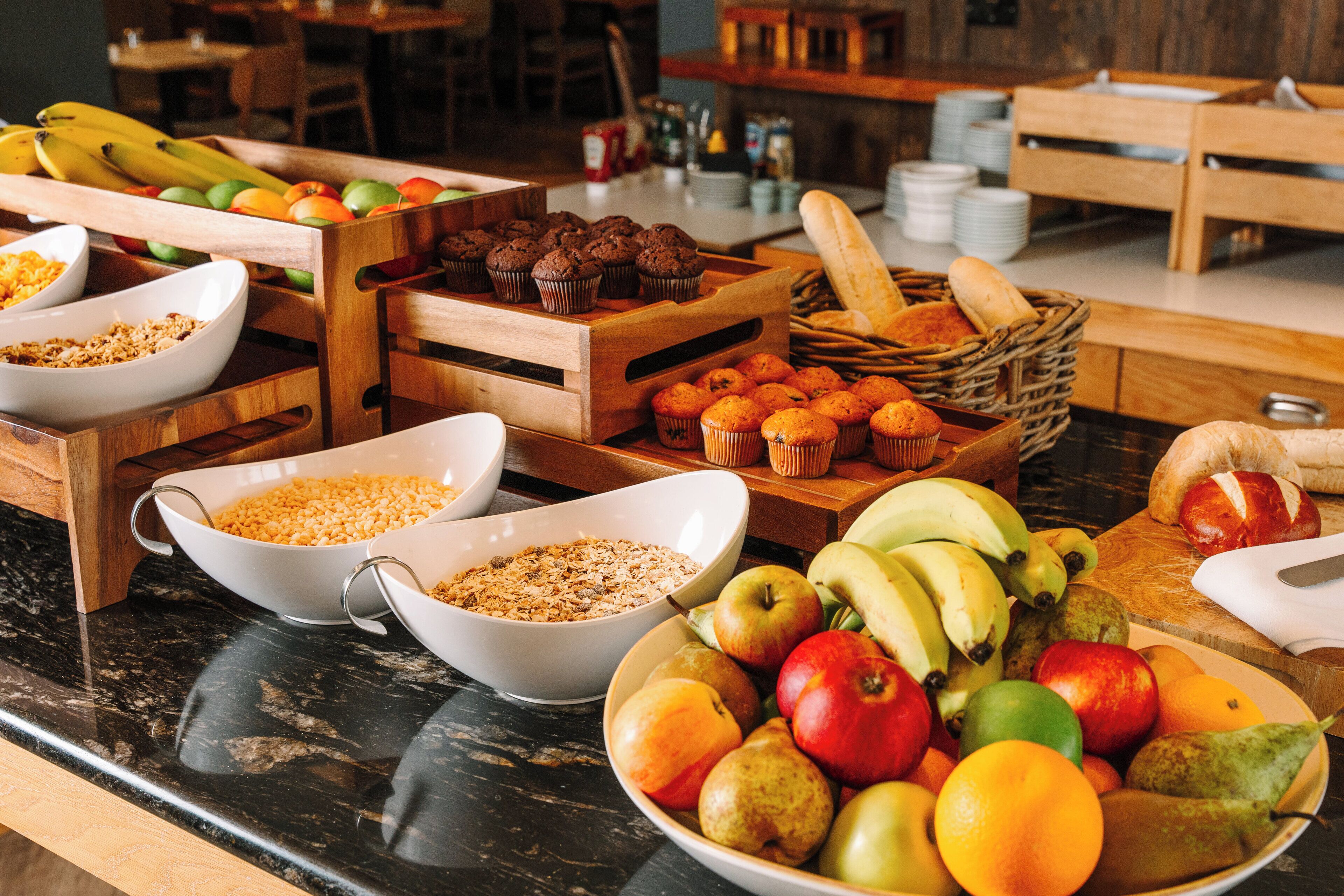 Un bufé con diversas opciones de comida, entre ellas frutas, muffins y pan.