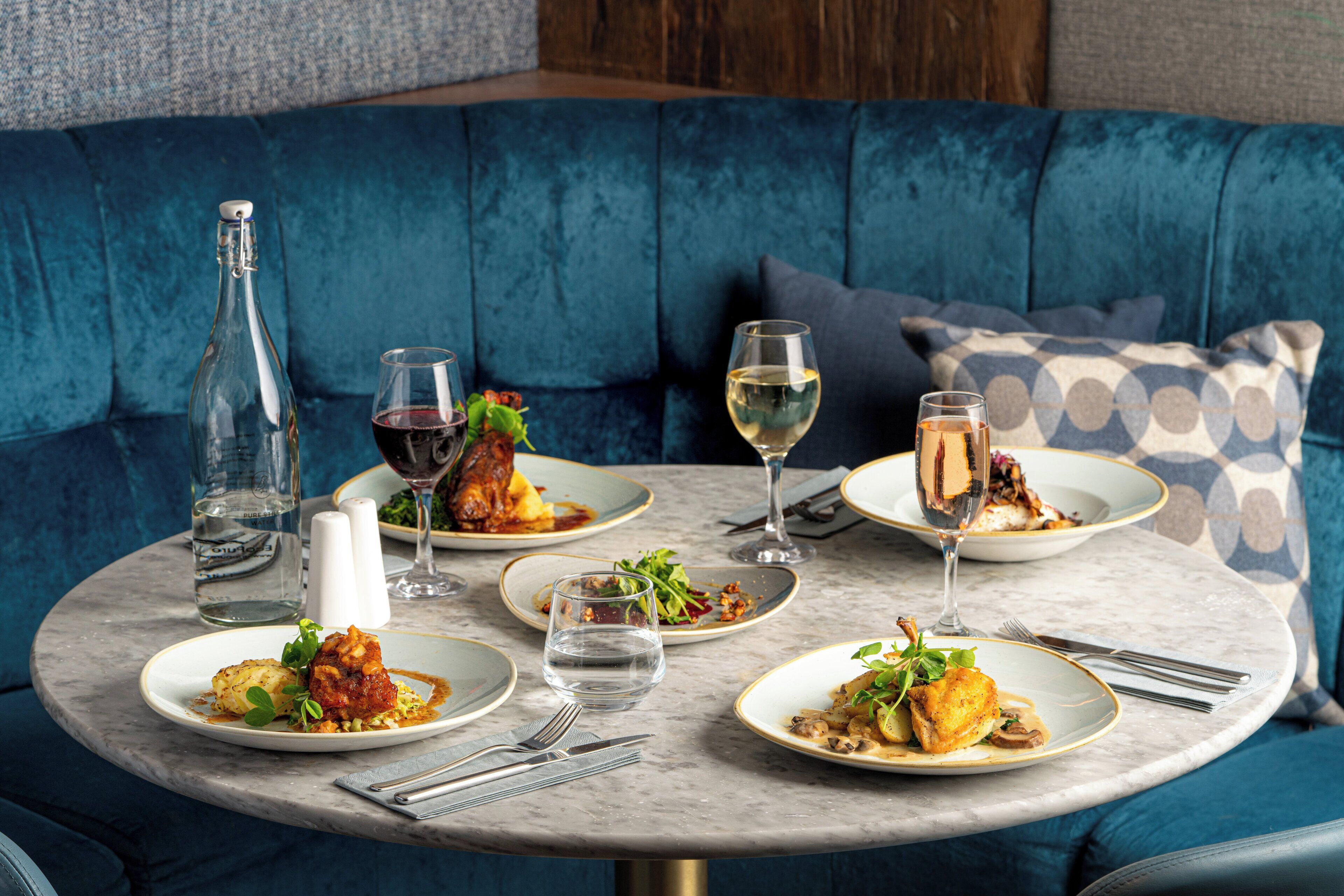 A round marble table set with plates of food, glasses of wine, and a bottle of water.