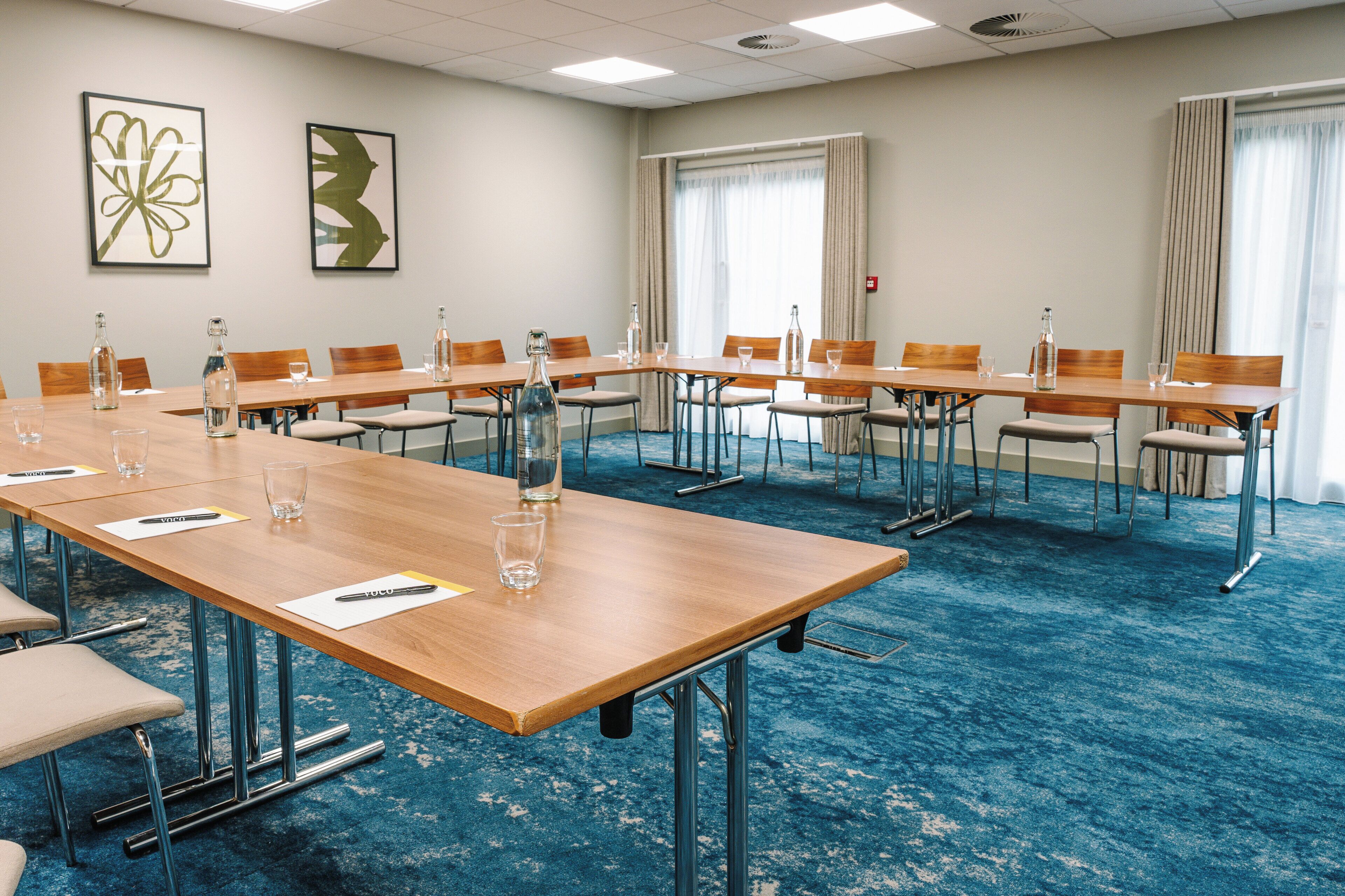 Une salle de conférence équipée de longues tables, de chaises et de bouteilles d’eau.