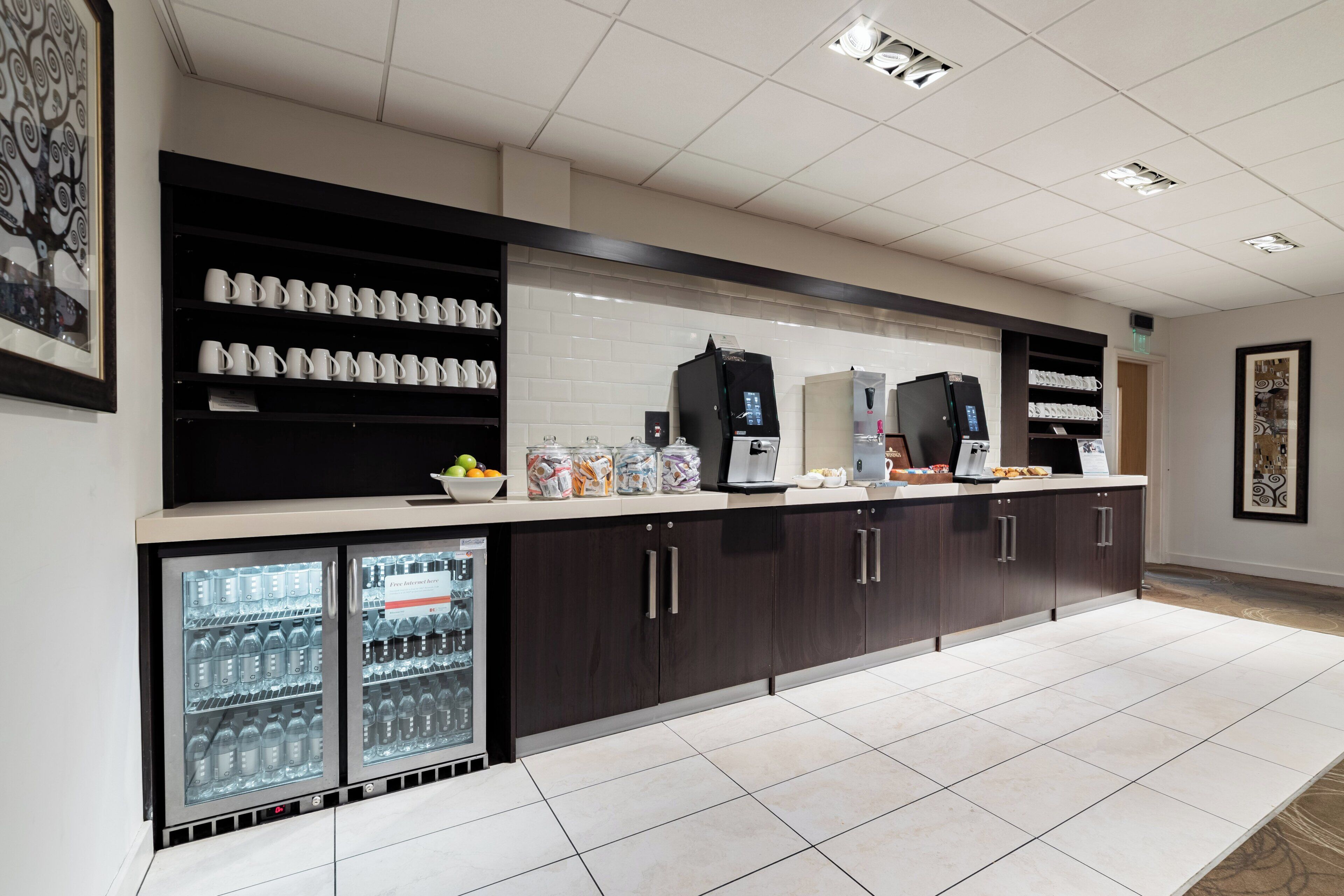 Een moderne keuken met een koffiehoek, gekoelde drankautomaten en diverse soorten eten.