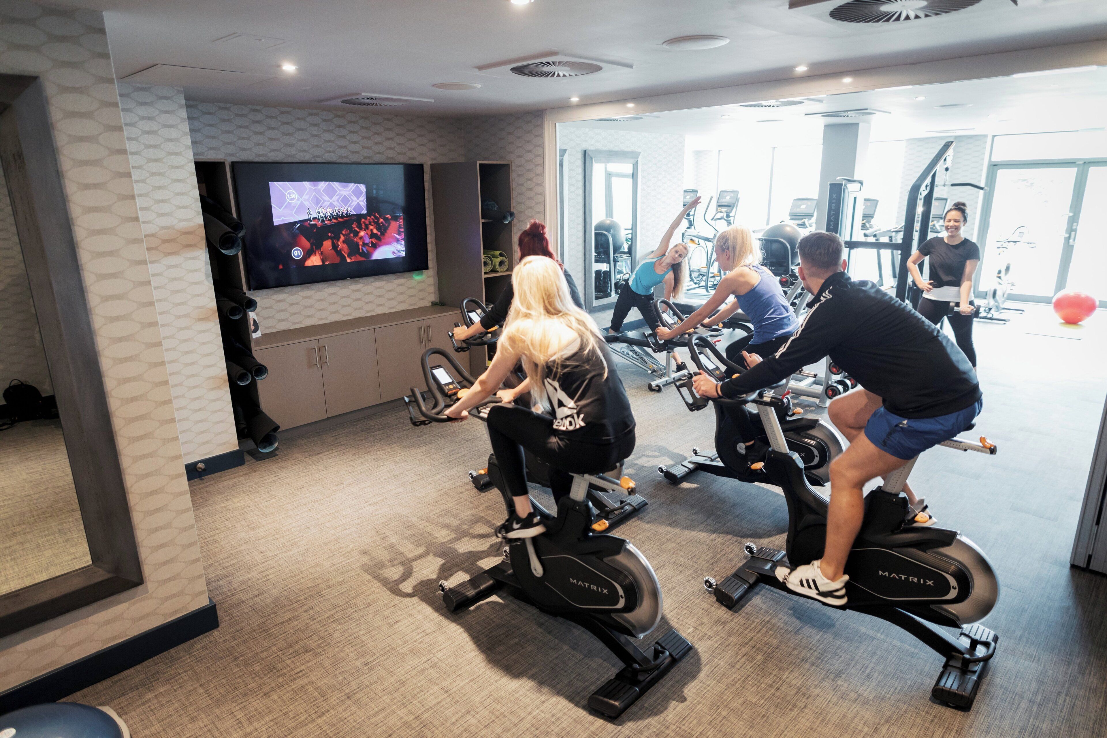 A gym with stationary bikes, a television screen, and exercise equipment.