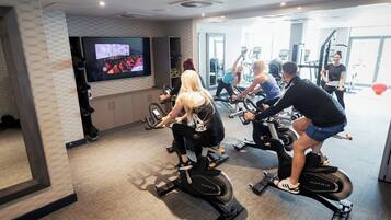 A gym with stationary bikes, a television screen, and exercise equipment.