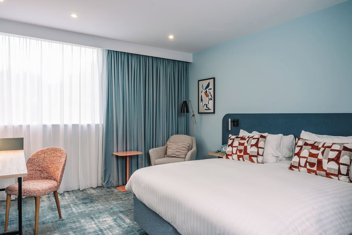 A hotel room with a large bed, a chair, a small table, and a desk.