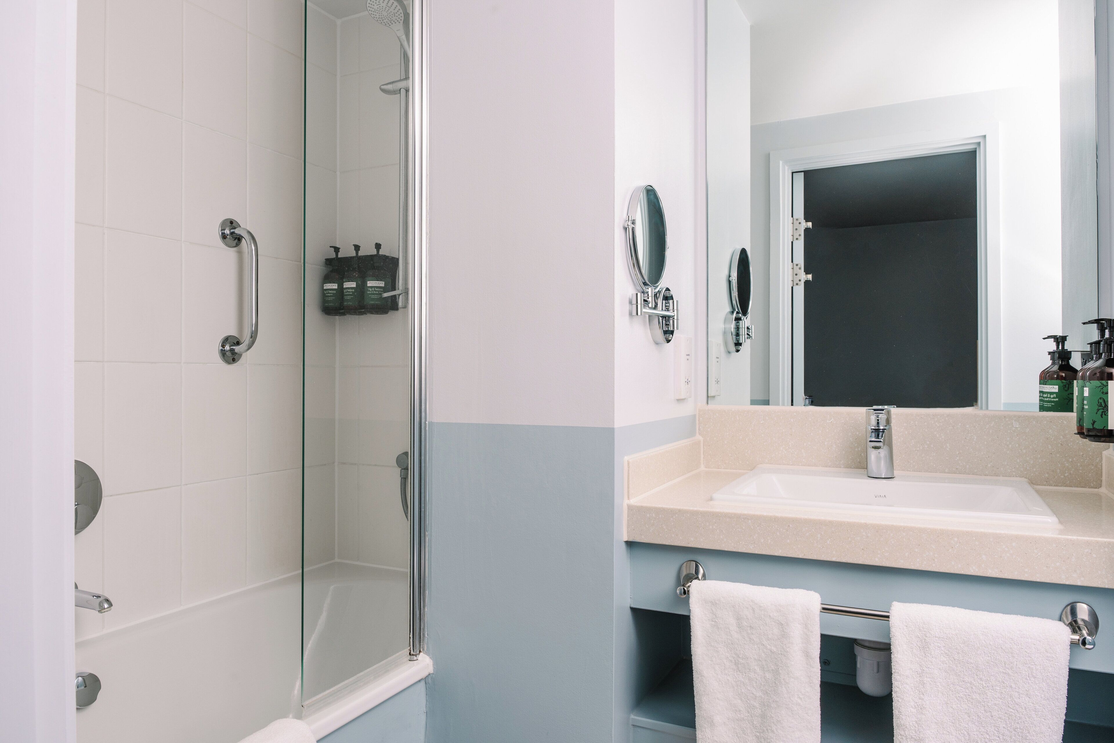 Un baño con cabina de ducha de vidrio, un lavabo con espejo y dos toallas sobre el mostrador.