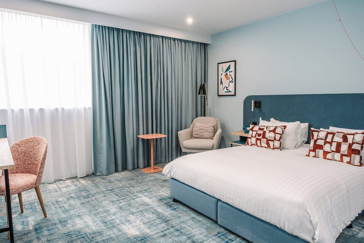 A hotel room with a large bed, a chair, a small table, and a lamp.