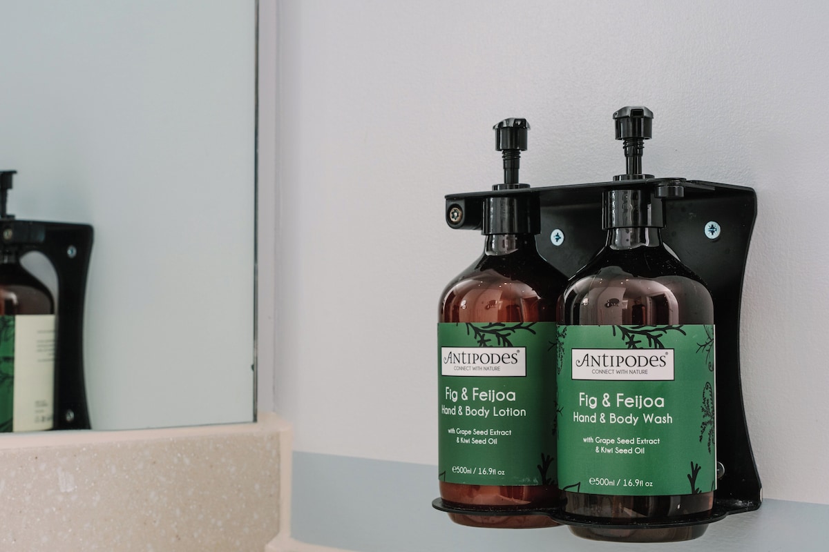 Deux bouteilles de lotion pour les mains et le corps et de gel nettoyant pour les mains et le corps, parfum figue et goyave, sont posées sur une étagère.