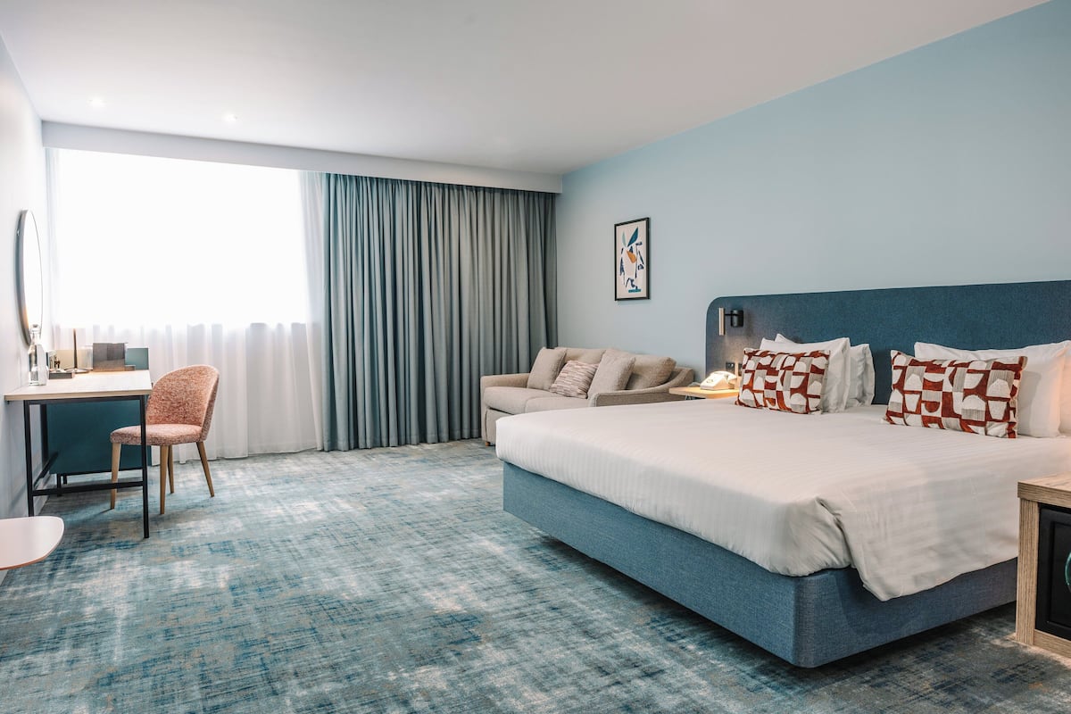 A modern hotel room with a large bed, a desk, and a chair.