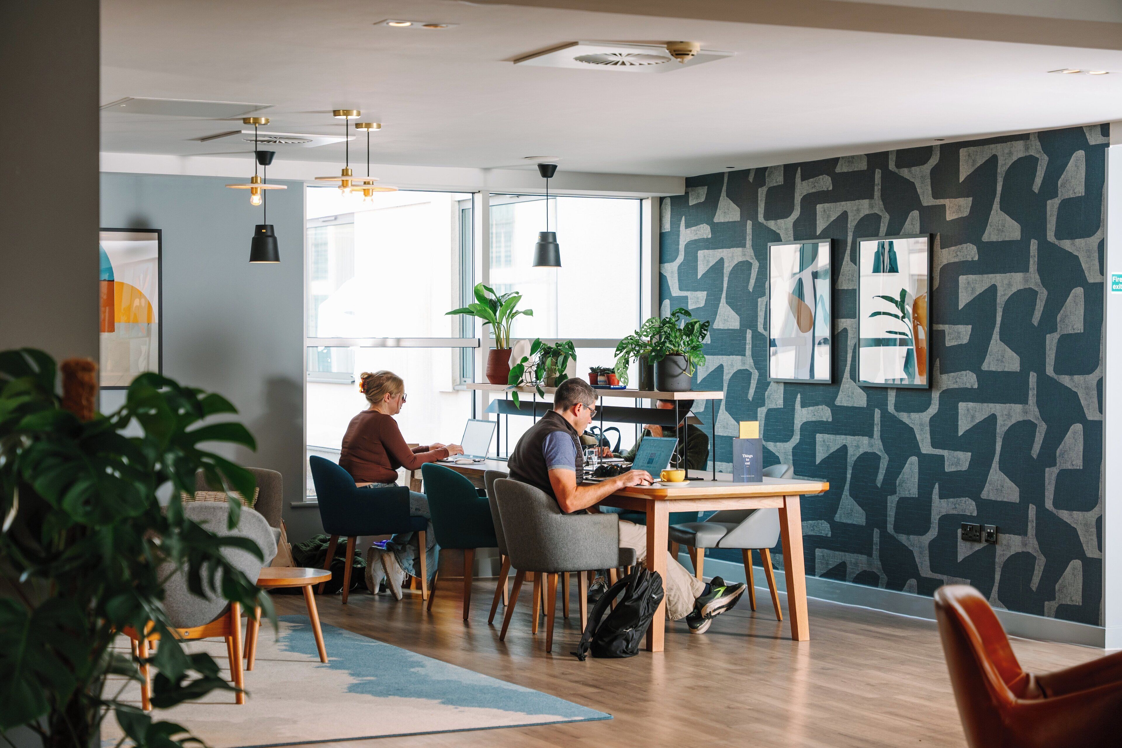 A modern office space with multiple workstations, large windows, and indoor plants.