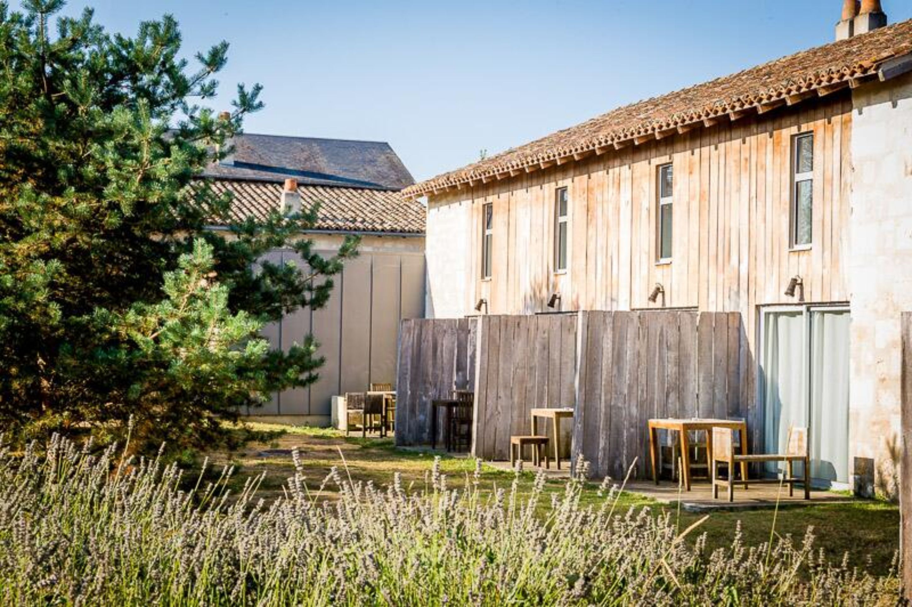 A rustic building with a wooden exterior, a tiled roof, and a fenced backyard with outdoor seating.