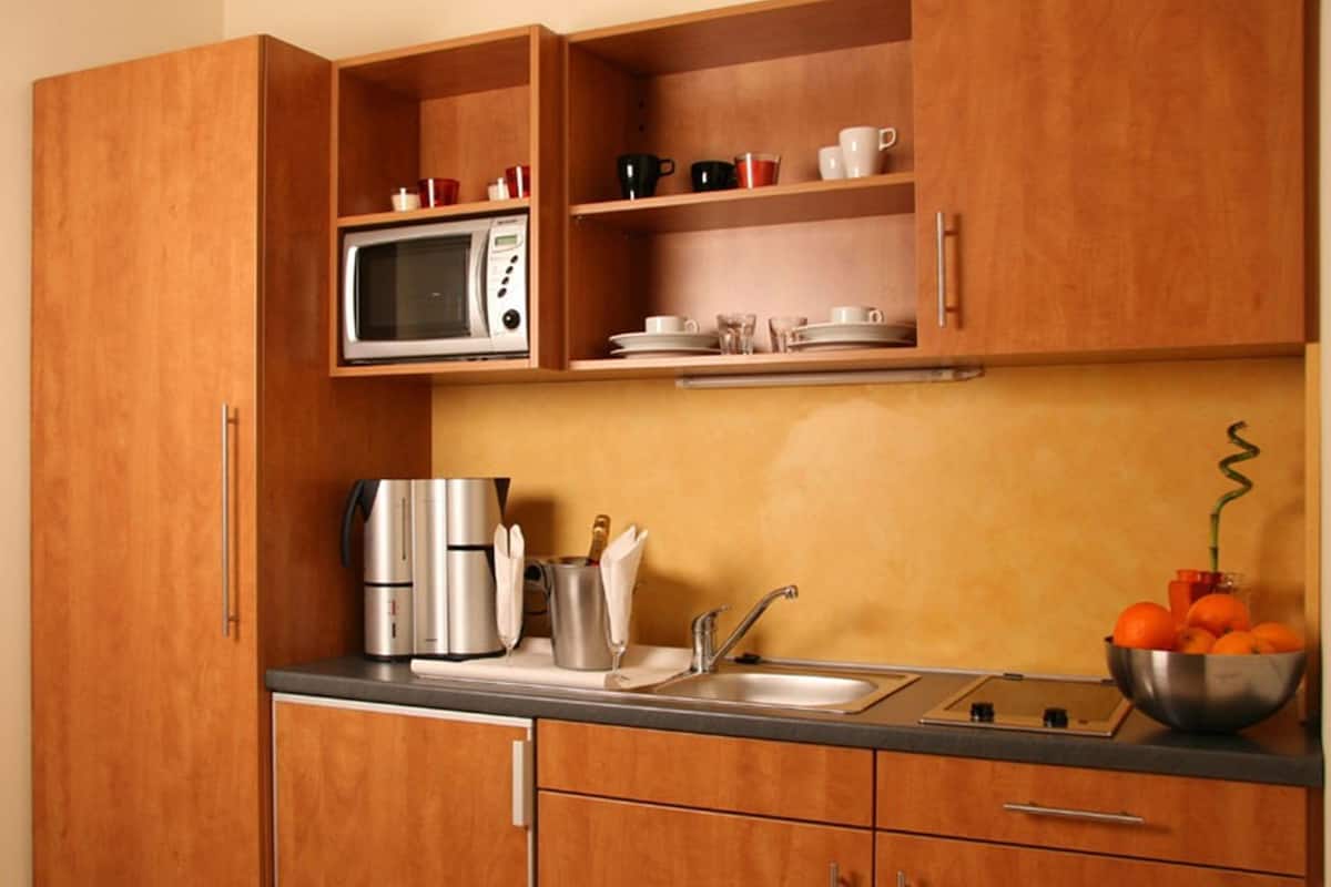 A kitchen with wooden cabinets, a microwave, a coffee maker, a sink, and a bowl of oranges.