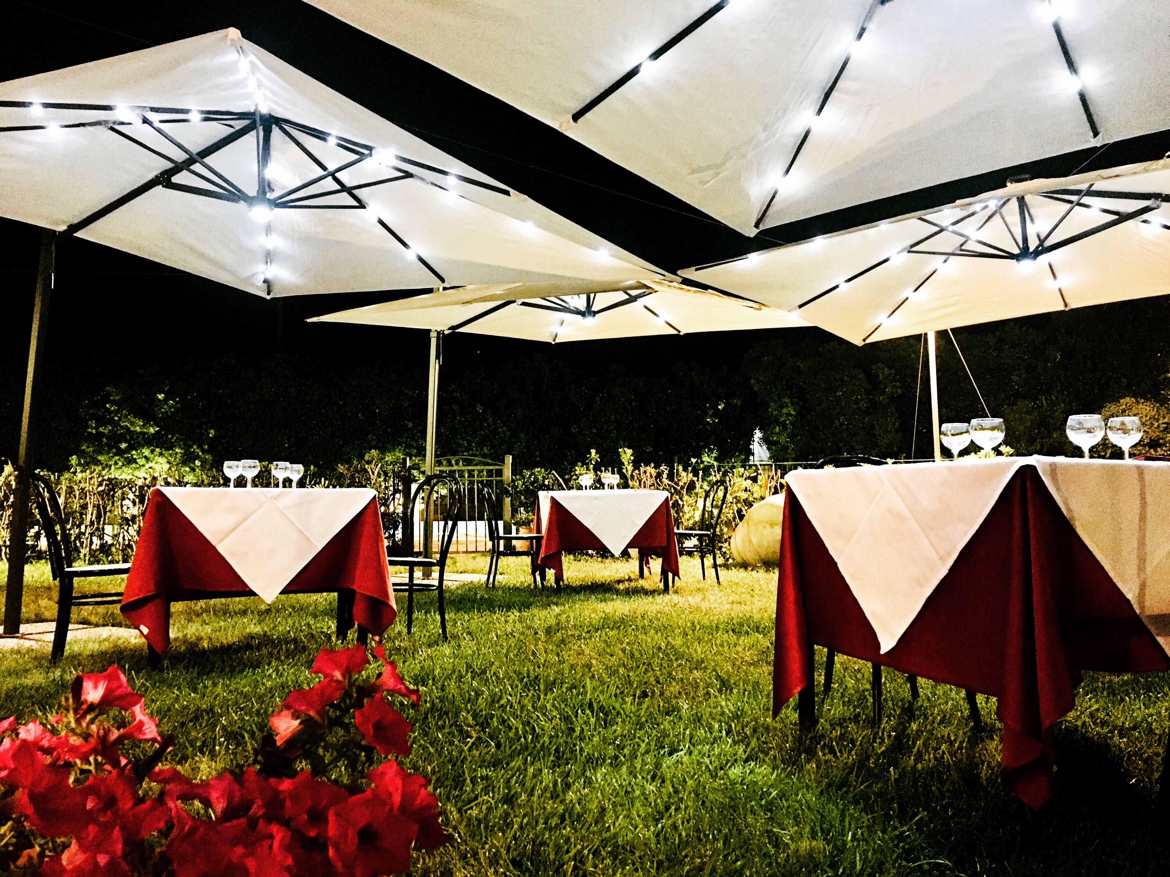 Outdoor tables with white canopies, red tablecloths, and chairs.