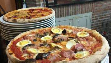 Dos pizzas sobre platos apilados frente a un horno de ladrillo.