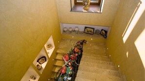 A staircase with a decorative garland, a window with a vase, and wall-mounted lamps. - Corte Aragonese (Santa Maria di Licodia)