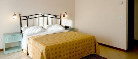 A bedroom with a bed, bedside lamps, a nightstand, a patterned bedspread, a rug, and a wooden ceiling.