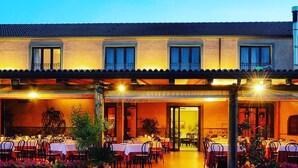 An outdoor dining area with tables and chairs, a covered patio, and a building with multiple windows. - Corte Aragonese (Santa Maria di Licodia)