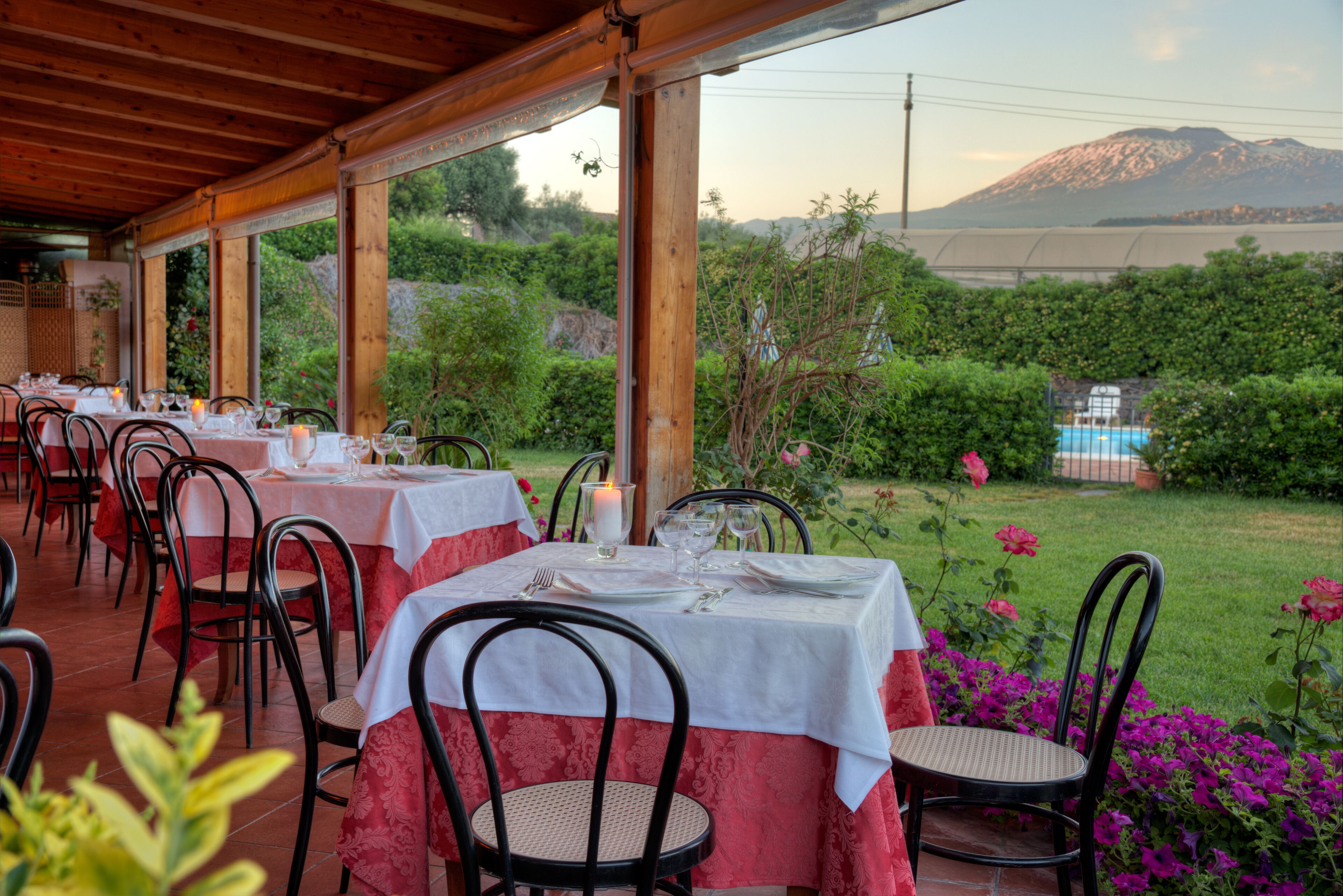 Un espace extérieur aménagé pour les repas, avec des tables pour deux personnes, entourées de chaises, et une vue sur une montagne en arrière-plan.