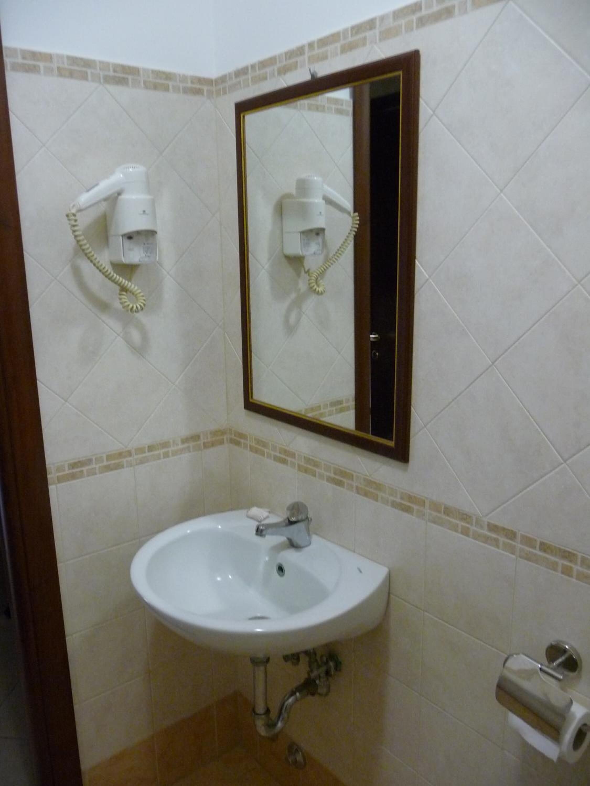 Un baño con un lavamanos blanco, un espejo y dos secadores de pelo fijados en la pared.