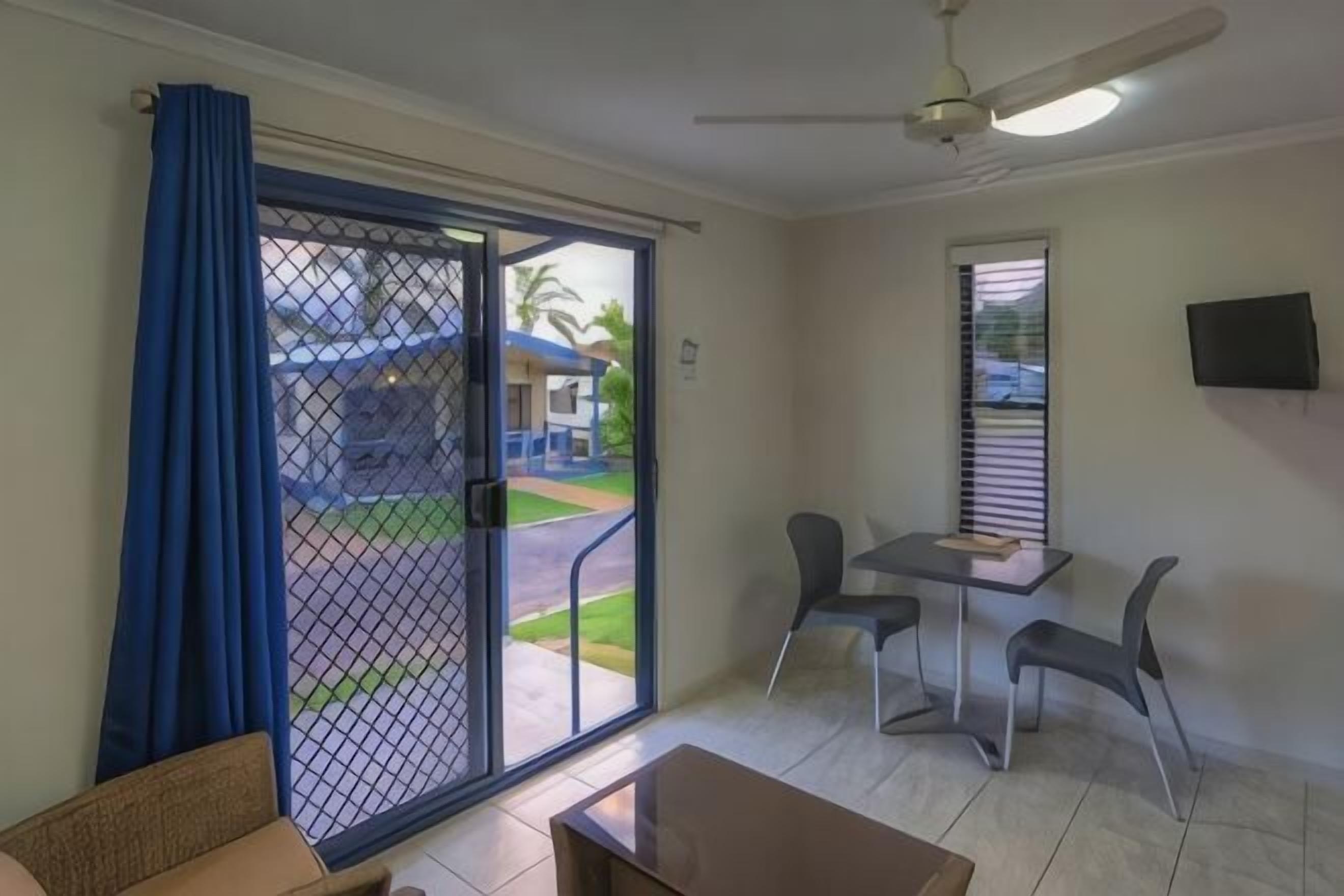 A room with a sliding glass door, a ceiling fan, a table with chairs, and a TV mounted on the wall.