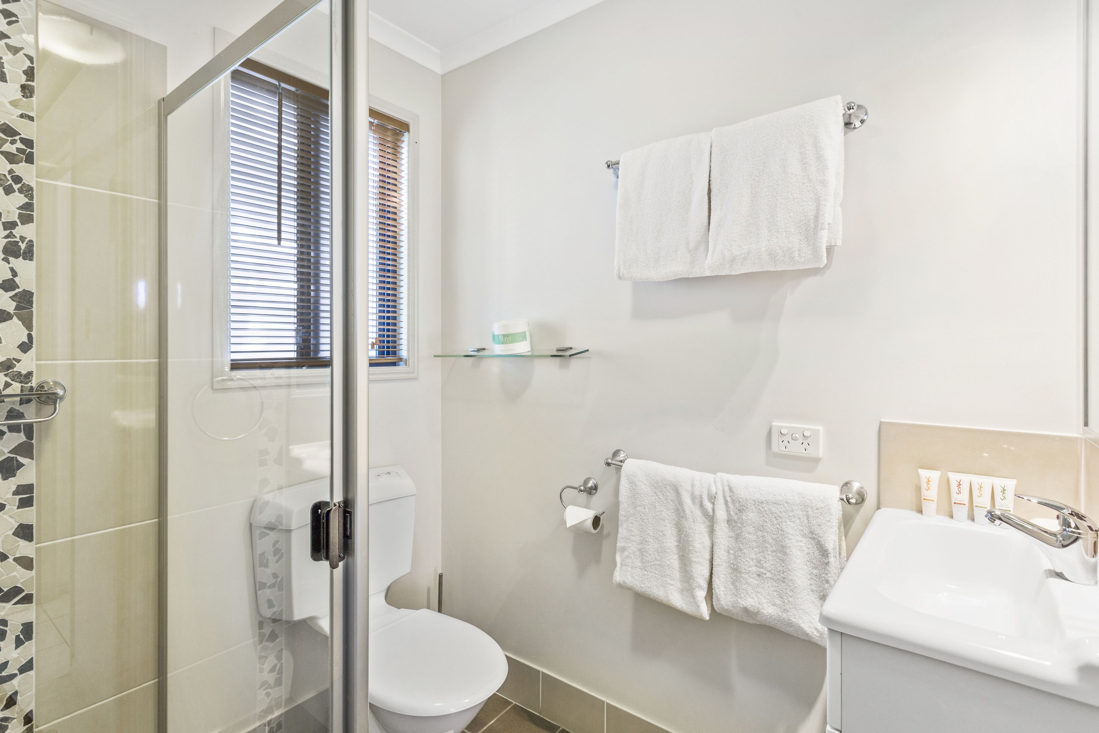 A bathroom with a glass shower enclosure, a toilet, a sink, and a towel rack.