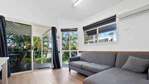 Quarto com sofá cinza, piso de madeira, porta de vidro deslizante e janela com persiana preta.