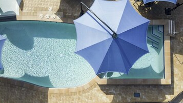 Una piscina con sombrilla azul, paredes con azulejos y suelo de ladrillo.