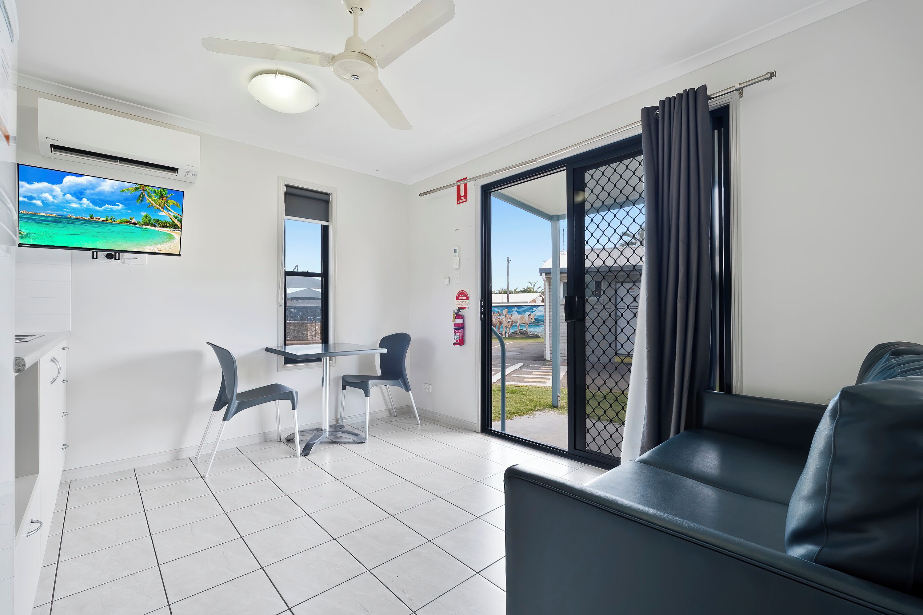 Una habitación moderna con ventilador de techo, televisión de pantalla plana, mesa de comedor con sillas, sofá y puerta corrediza de vidrio que da a un área exterior.