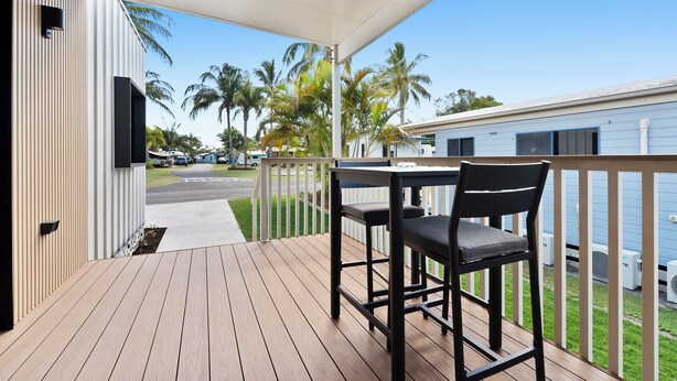 Um deck de madeira com mesa e cadeiras, com vista para uma rua com palmeiras e um edifício azul.