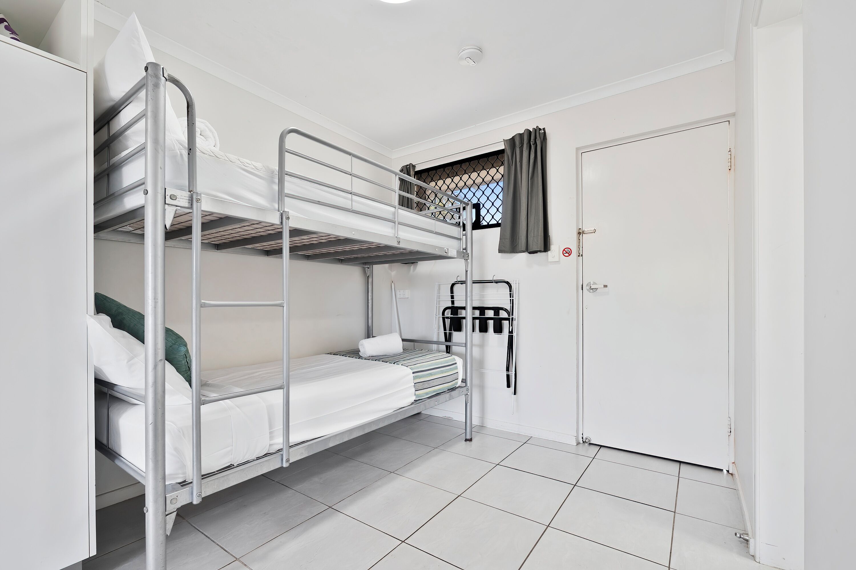 A bunk bed room with a door, a window with curtains, and a tiled floor.