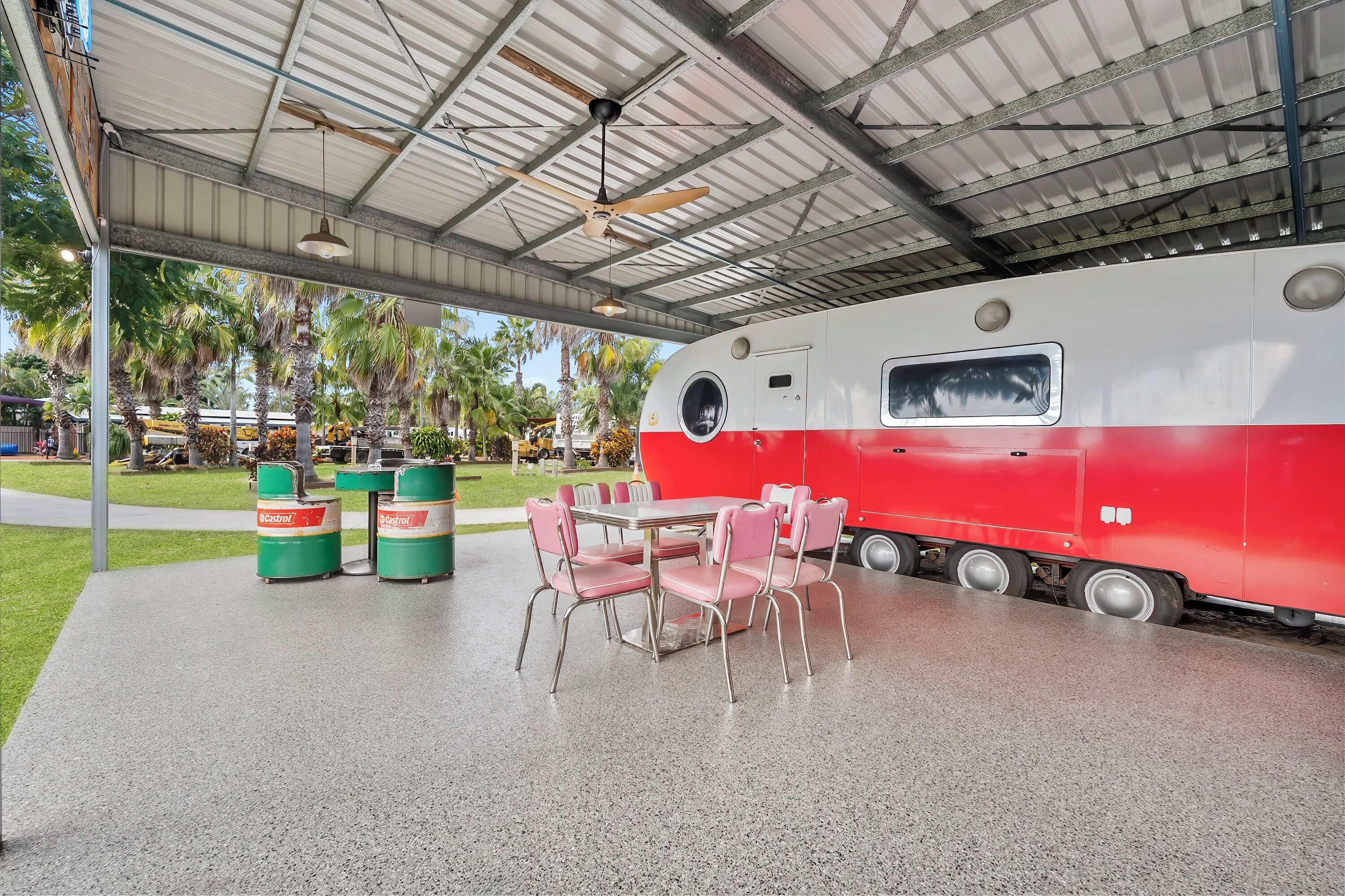 A covered outdoor area with a table and chairs, a red and white train, and green trash bins.