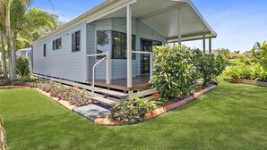 Uma casa móvel com varanda coberta, rodeada por paisagismo bem cuidado e palmeiras.