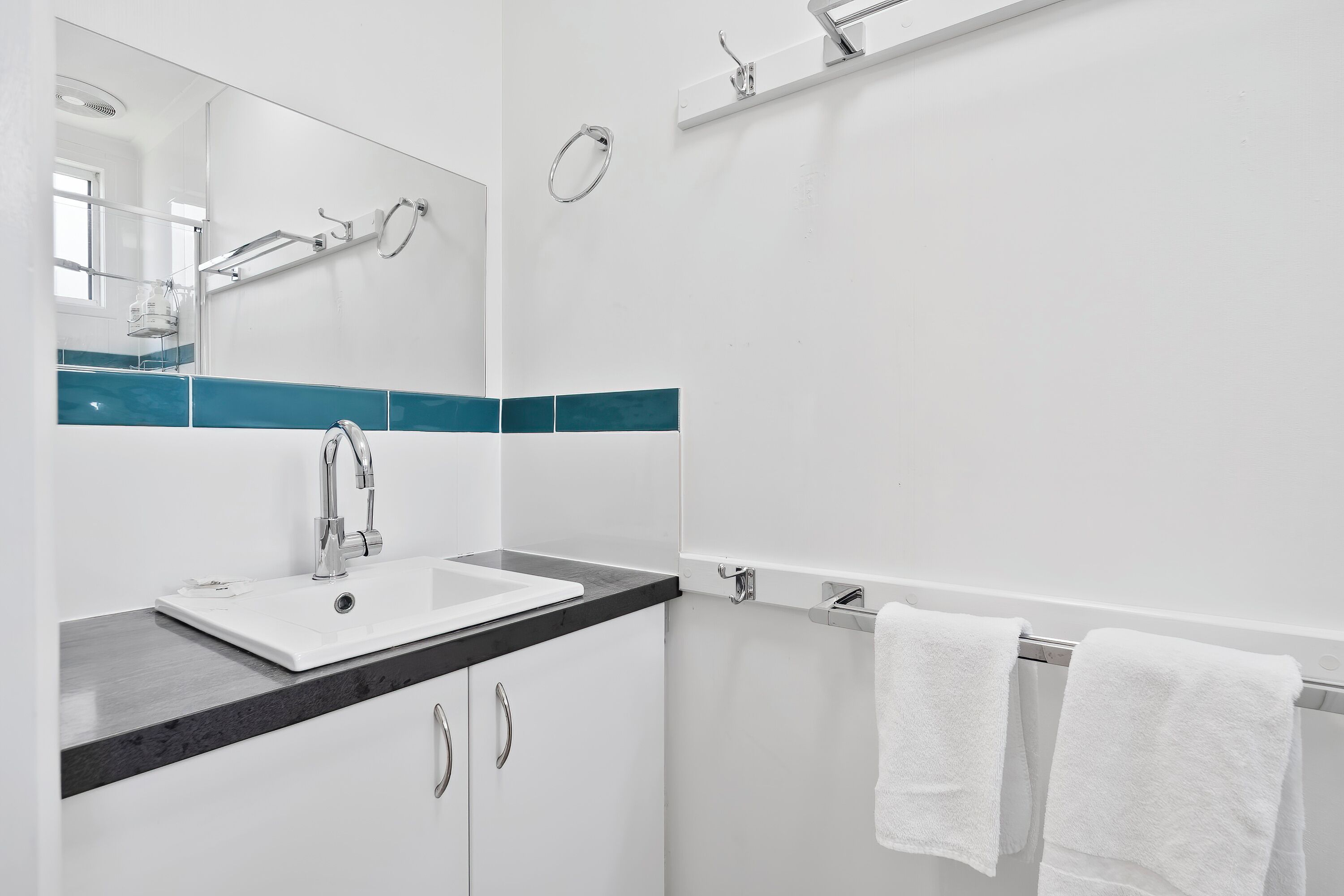 Ein modernes Badezimmer mit einem weißen Waschbecken, einer schwarzen Arbeitsplatte und einem Spiegel darüber.