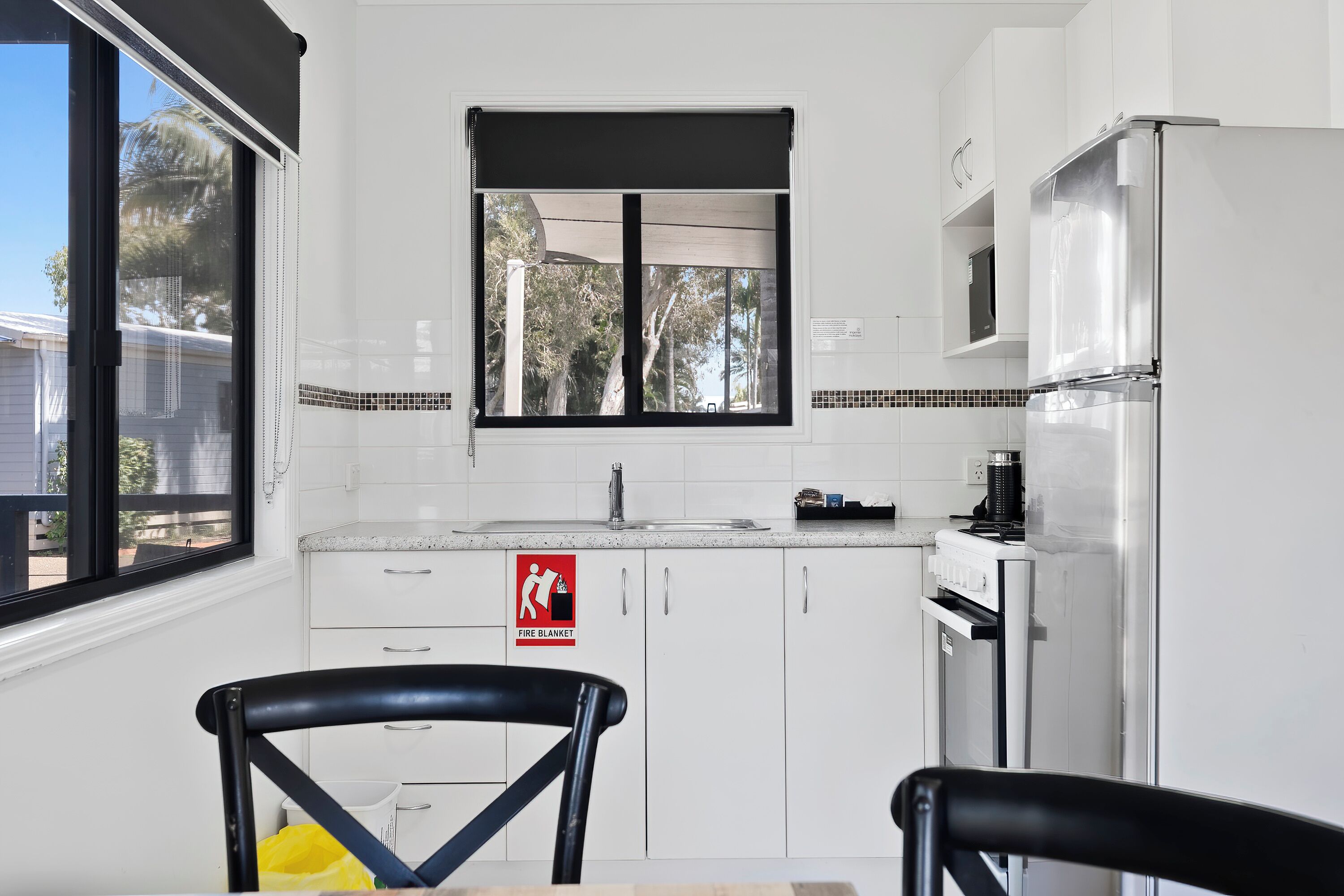 A kitchen with white cabinets, a stainless steel refrigerator, a window with a view of trees, and a fire blanket sign.