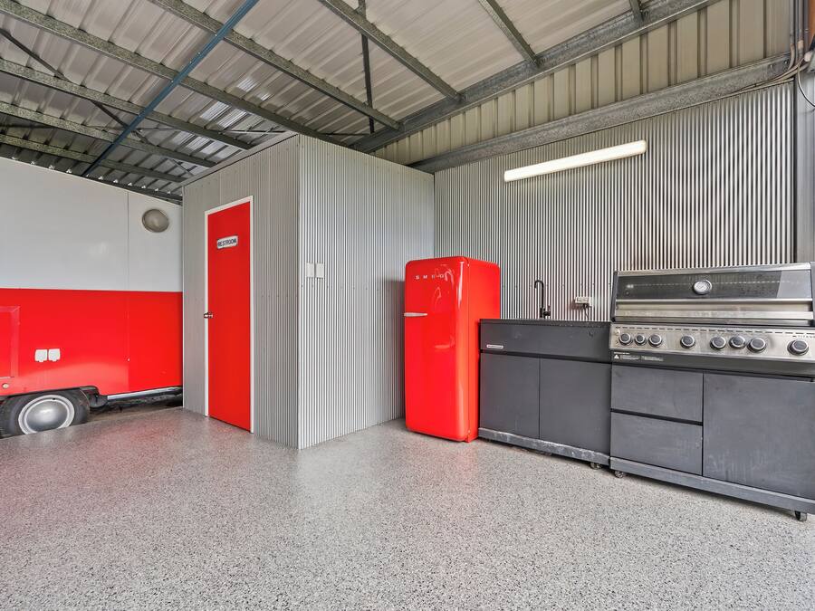 Zona de cuina amb un frigorífic vermell, un forn d'acer inoxidable i una porta amb la inscripció 'RESTROOM'.