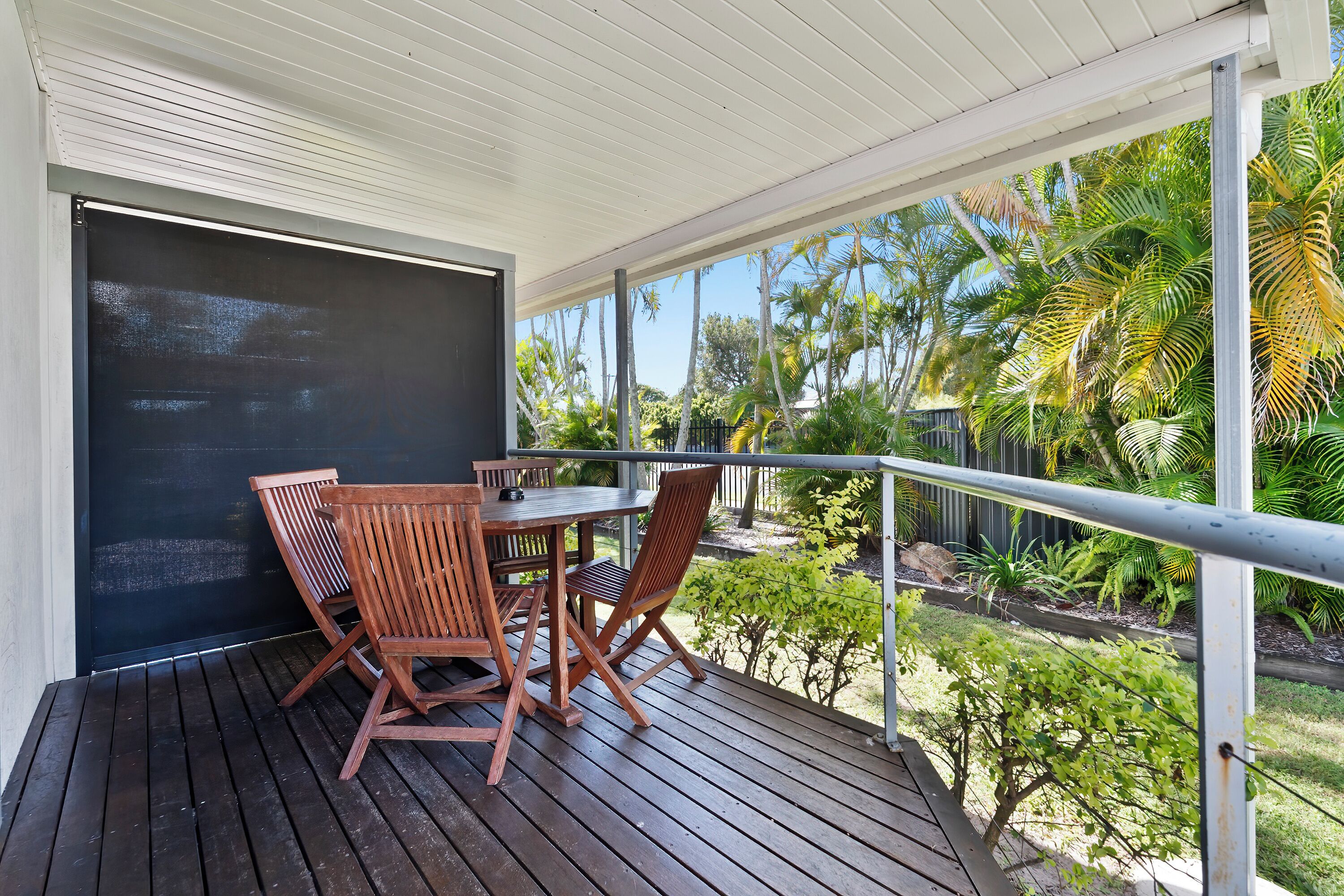 A covered outdoor area with a table and chairs, a black door, and a view of palm trees and greenery.