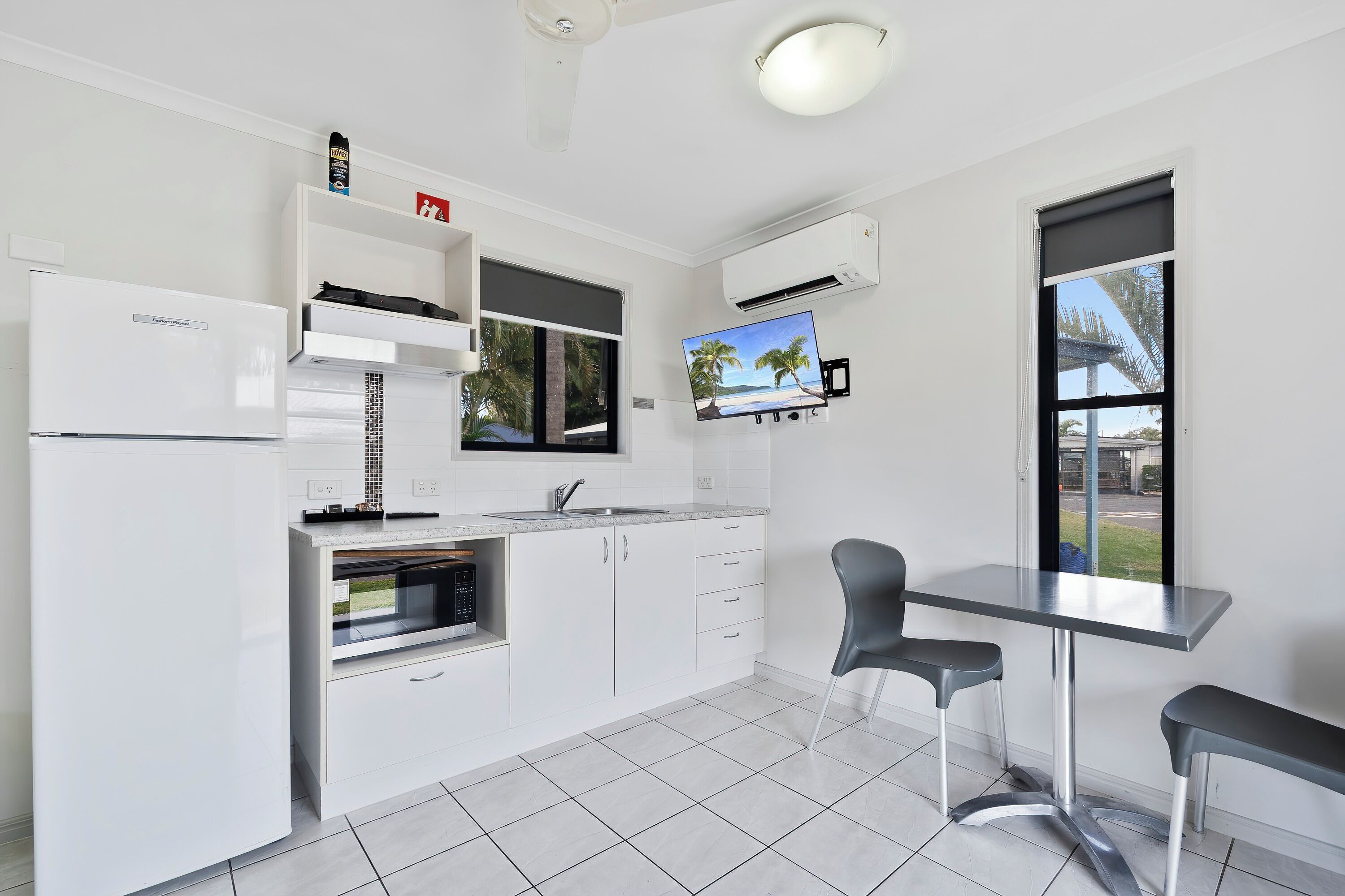 A modern kitchen with white cabinetry, a built-in oven, a sink, and a flat-screen TV mounted above it.