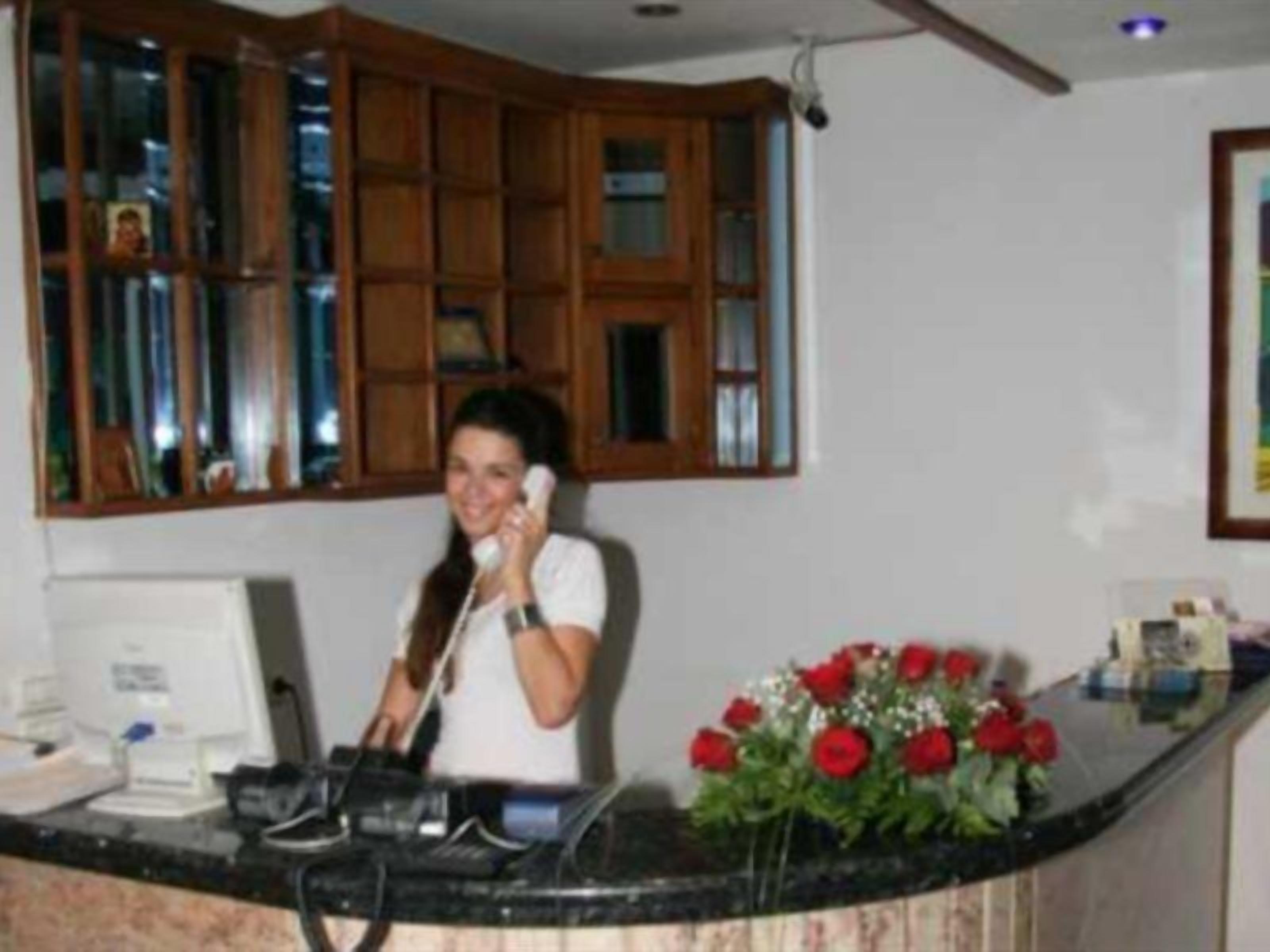 Eine Person steht an einem Schalter mit einem Computermonitor und einem Telefon. Ein Blumenstrauß mit roten Blumen steht auf dem Schalter.